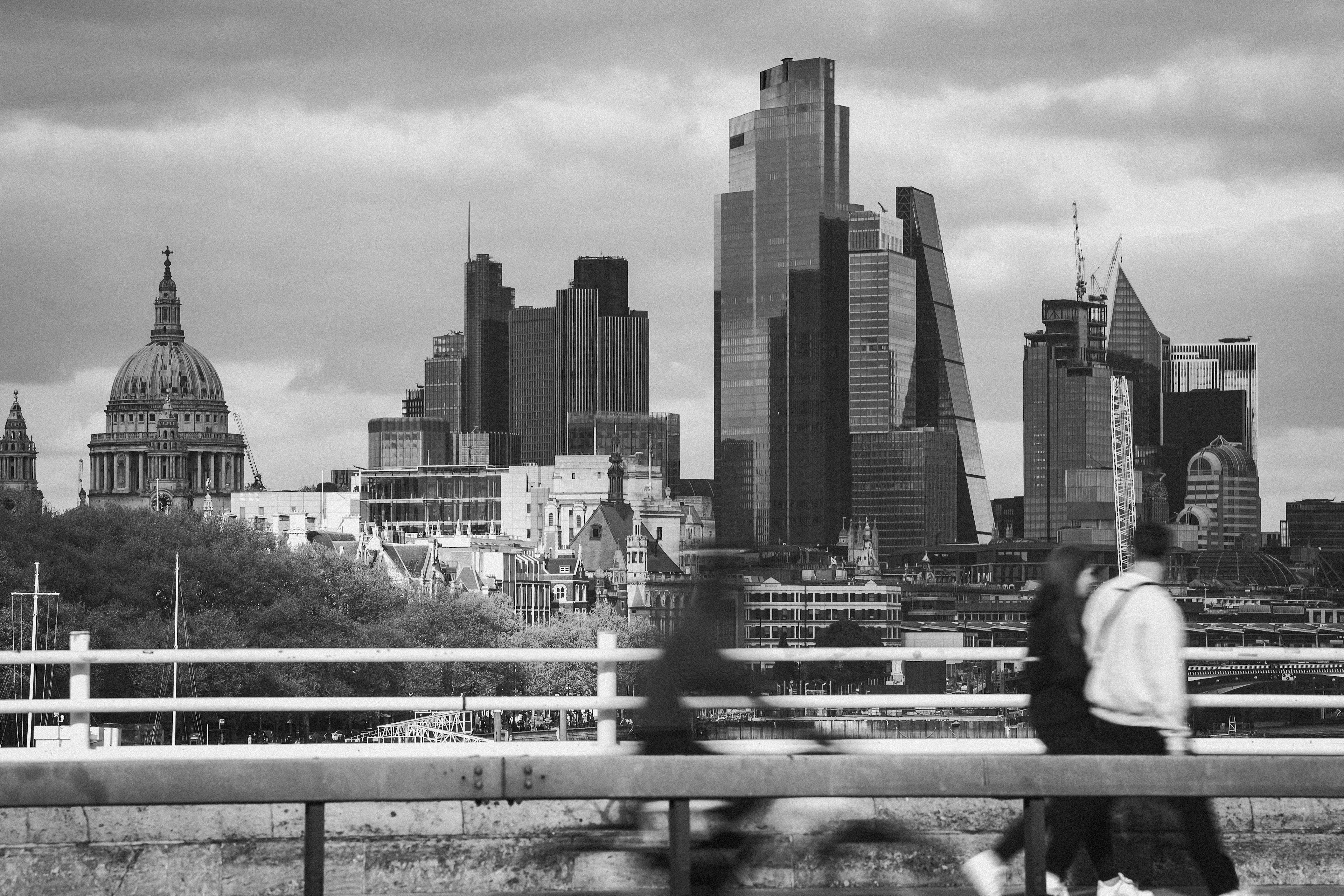 A monochrome view of London's skyline featuring iconic architecture with blurred pedestrians in the foreground.