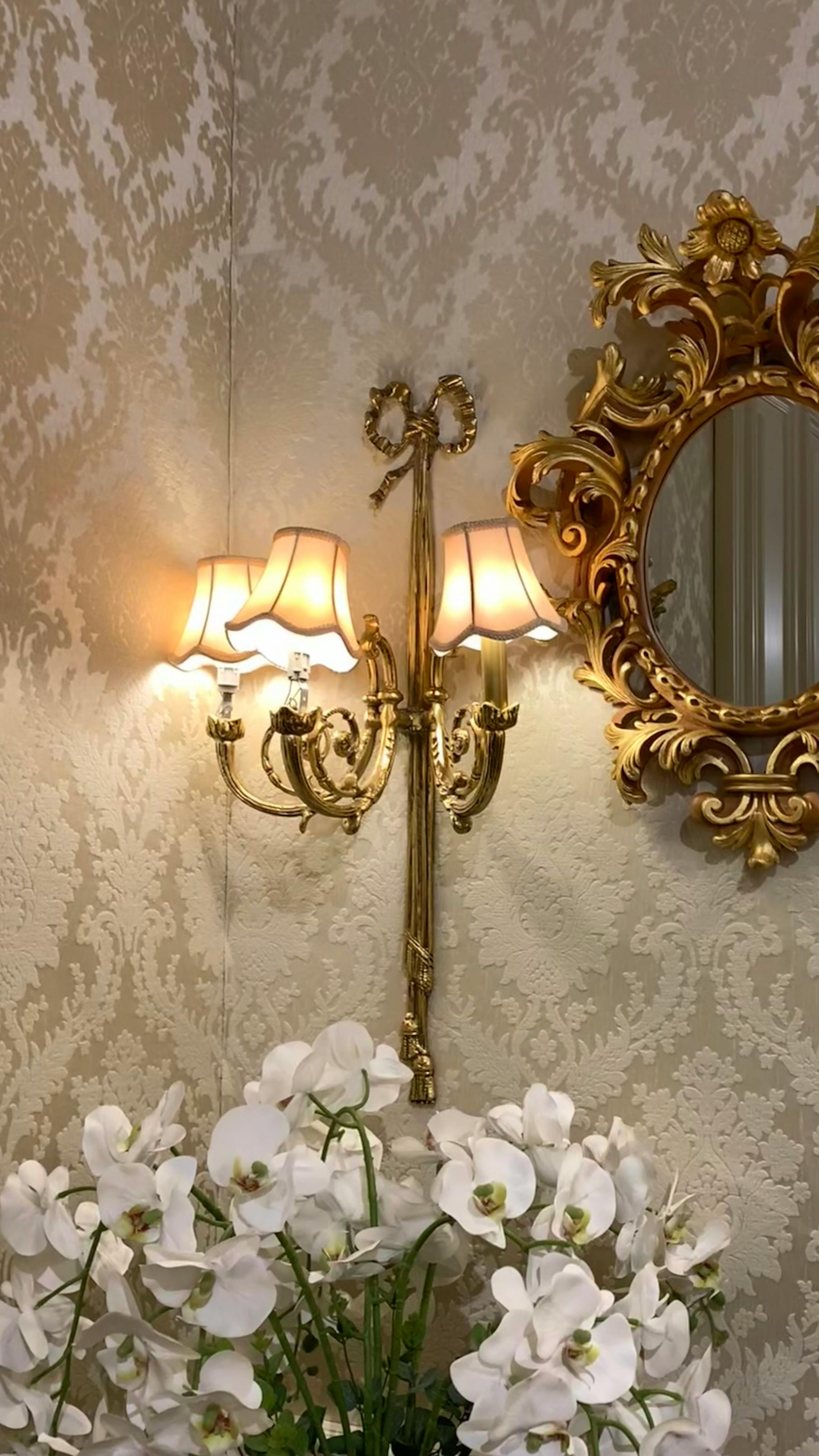 Ornate gold wall lamp and mirror enhancing vintage floral decor.