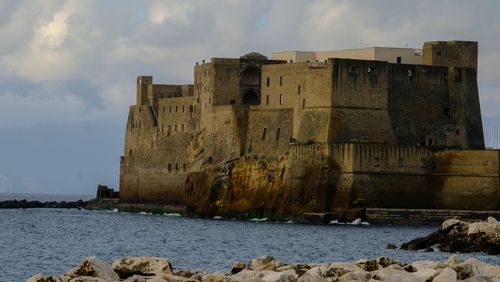 Free Scenic view of Castel dell'Ovo in Naples, Italy, with rocky shore and clouds. Stock Photo