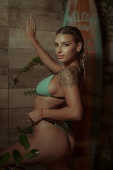 A woman in a bikini poses confidently beside a surfboard, exuding summer vibes.