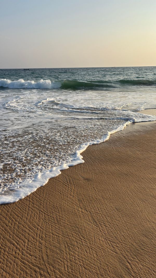 Cena tranquila de praia ao pôr do sol com ondas suaves e areia dourada.