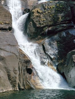 A tranquil waterfall flowing over rocky cliffs into a calm pool below, captured in daylight.