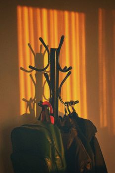 Coat rack with jackets and bags casting shadows in warm sunset light.
