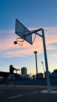 A boy shooting a basketball outdoors in İstanbul at sunset. Silhouette against a vibrant sky.