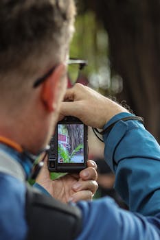 Man photographing nature with camera outdoors, focusing on vibrant greenery.