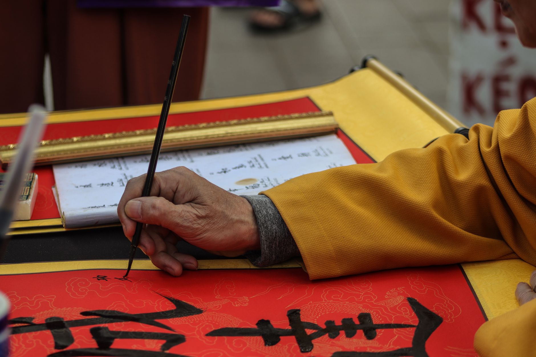 A person practicing traditional Chinese calligraphy with a brush on a red mat.
