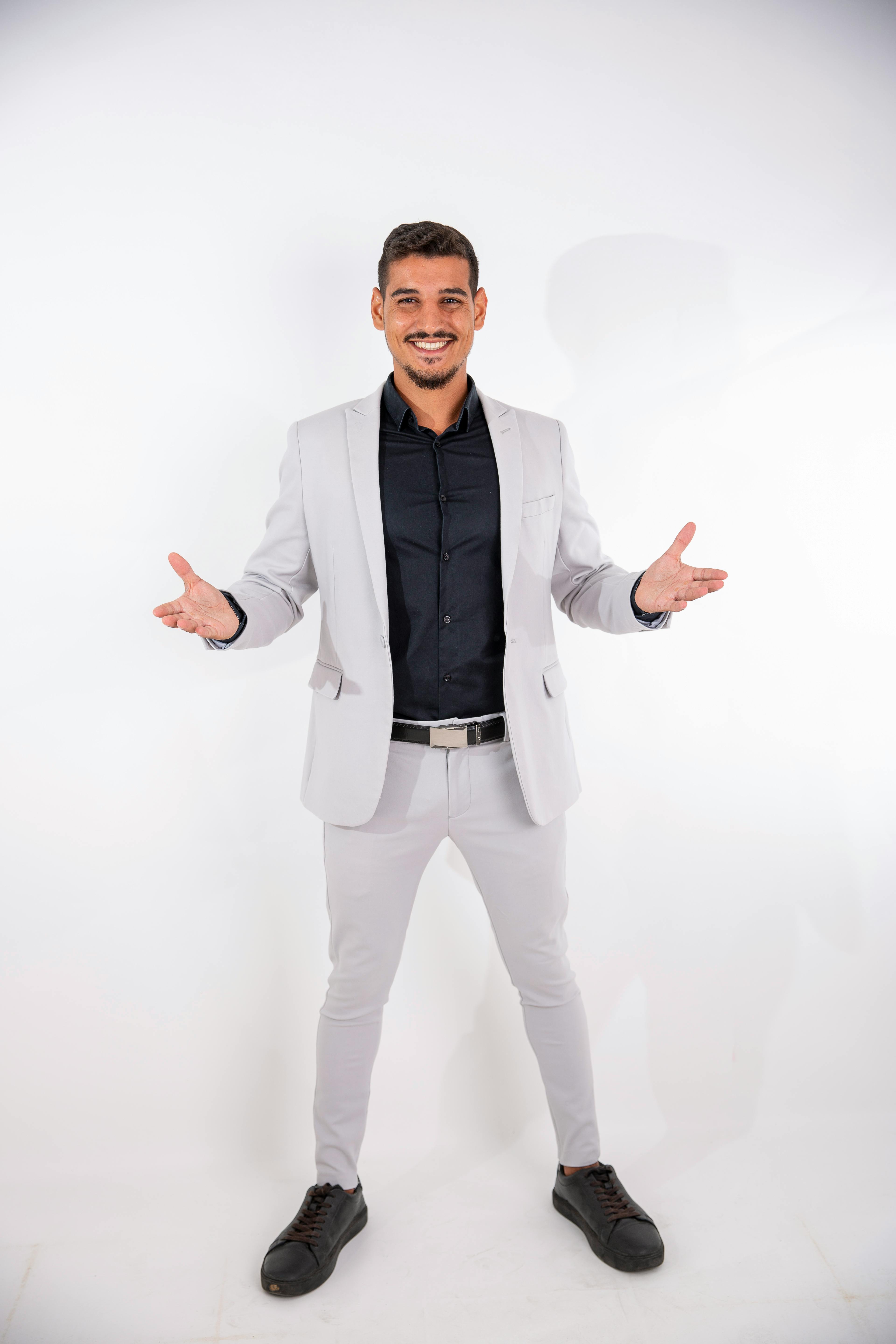 Portrait of a confident young man smiling in a stylish black and white suit against a white background.