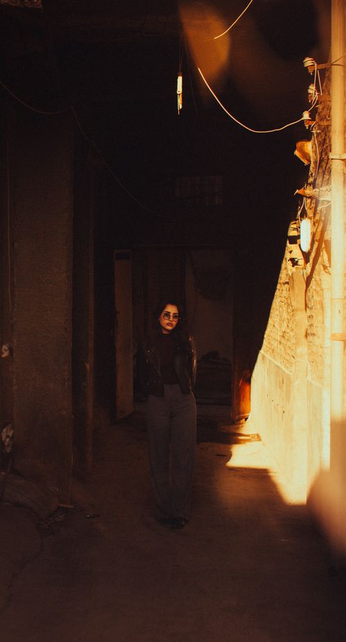 Free A mysterious woman stands in a shadowy alley, lit by warm sunlight. Stock Photo