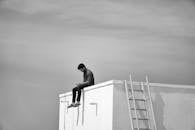 Solitary adult sitting on rooftop edge