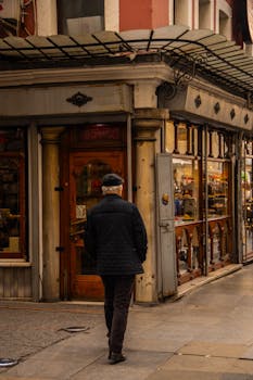 Elderly man in casual attire walking past a vintage urban shop. City life captured in a warm tone.