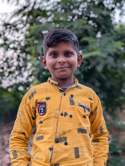 Free Portrait of a joyful young child posing in a bright yellow shirt with trees in the background. Stock Photo