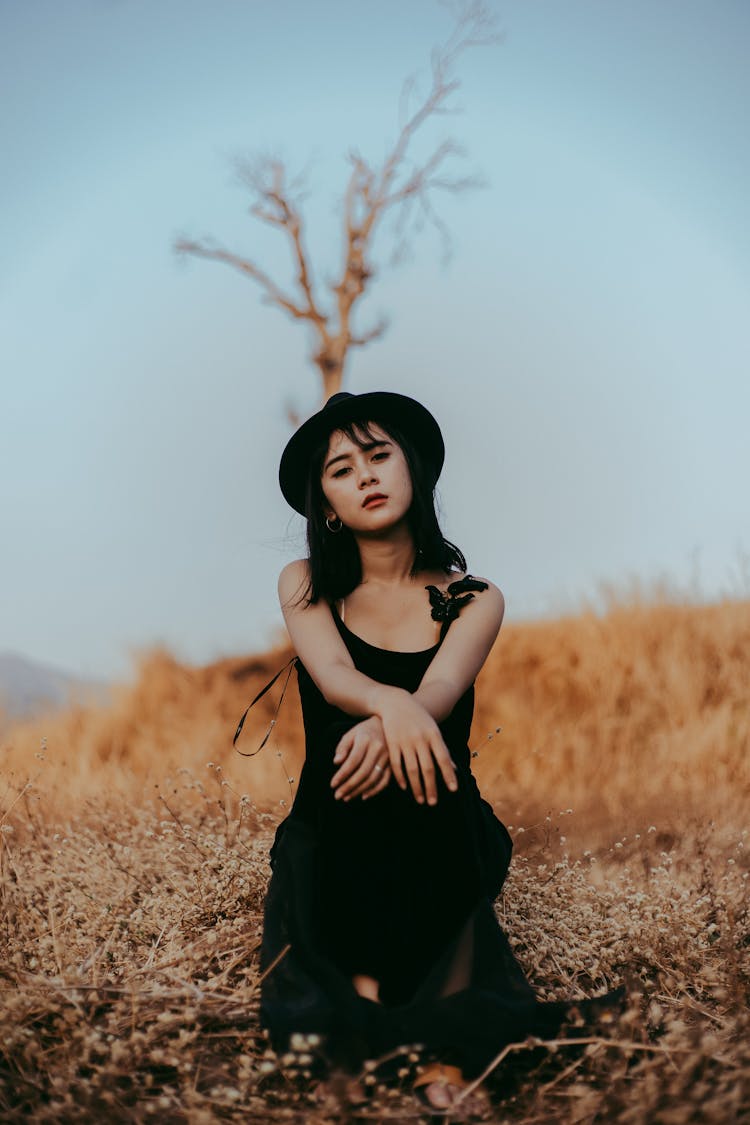 Woman In Black Sleeveless Dress Sitting Outdoors