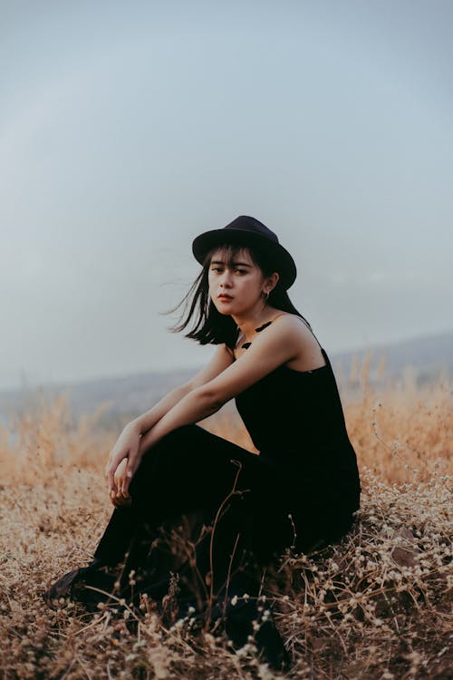 Femme Assise Portant Une Robe Sans Manches Noire Entourée D'herbe à Feuilles Vertes