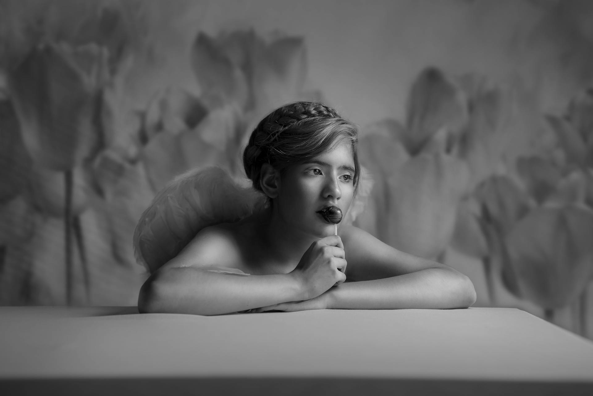 Black and white portrait of a young girl with angelic wings and lollipop.