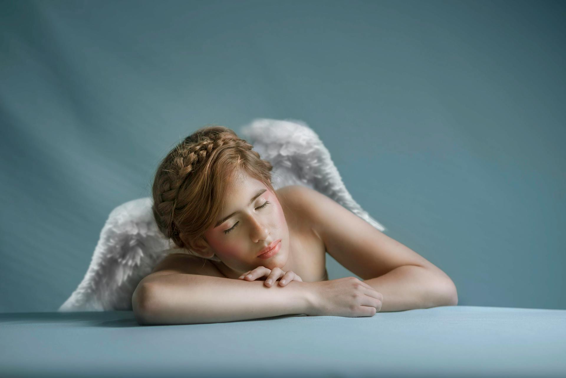 Peaceful angelic figure with white wings resting on a soft surface, conveying tranquility.