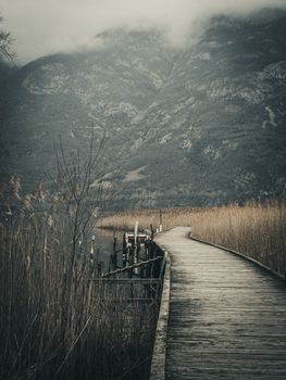 A tranquil boardwalk leading through a serene landscape with misty mountains in Italy.