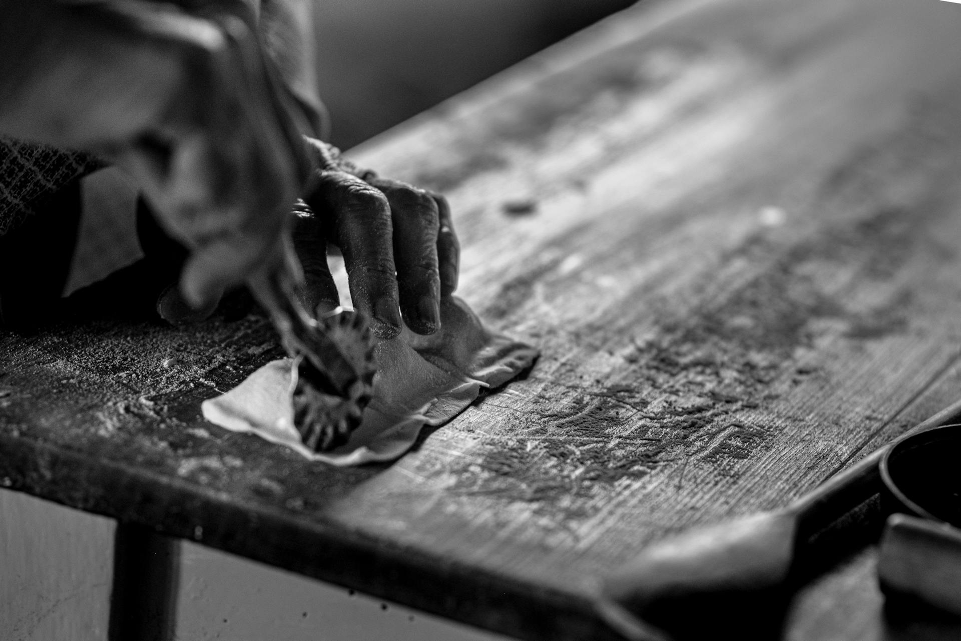 A close-up of hands crafting dough on a wooden table in black and white.