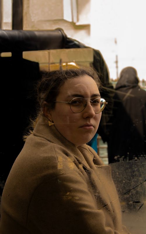 Free A woman in a coat reflected in glass with a thoughtful expression. Urban setting. Stock Photo