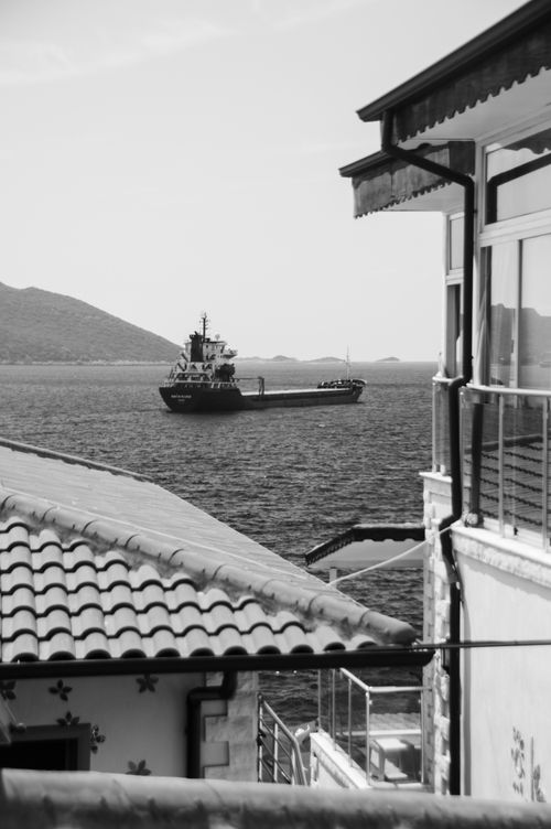 Free A serene black and white view of a ship at sea framed by rooftops and buildings. Stock Photo