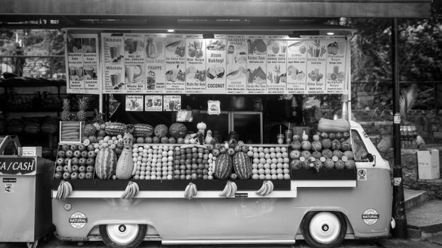 Monochrome image of a colorful fruit stand with various signs and fresh produce.