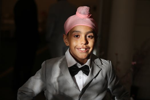 Cheerful boy wearing a pink turban and a suit smiling warmly indoors.