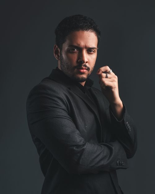 Free Portrait of a confident young man in a formal black suit, posing thoughtfully against a dark background. Stock Photo