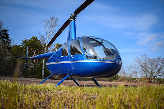 Low angle view of a blue helicopter on a grassy field under a clear blue sky.