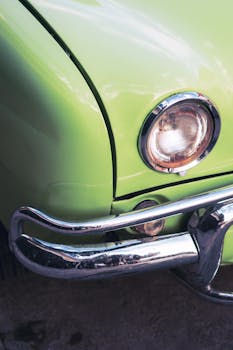 Close-up shot of a vintage green car's headlight and chrome bumper.