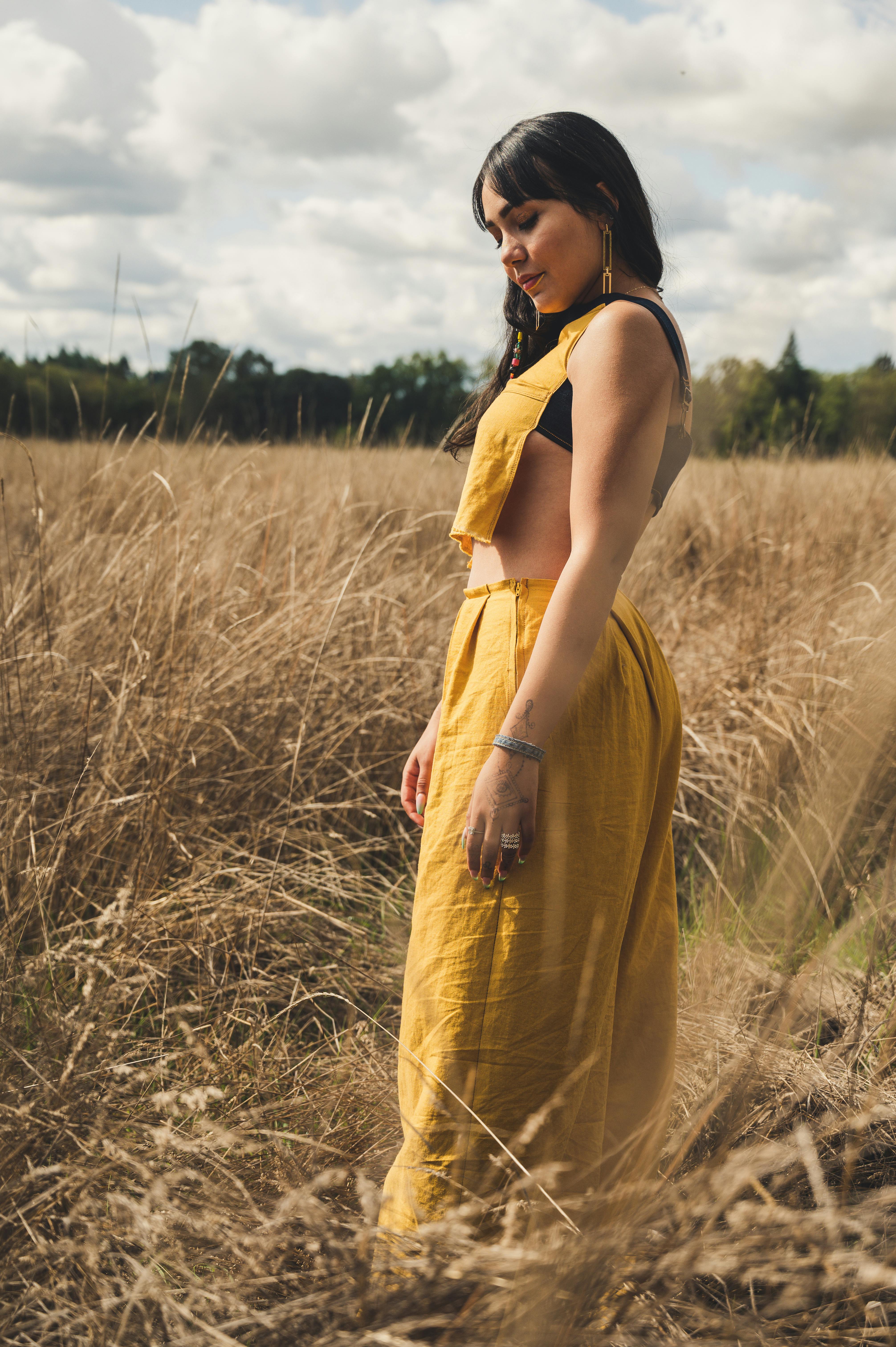 一位身着亮黄色服装的女子在阳光照耀的田野间优雅伫立，展现出自然之美与时尚气息