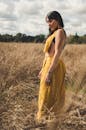 一位身着亮黄色服装的女子在阳光照耀的田野间优雅伫立，展现出自然之美与时尚气息