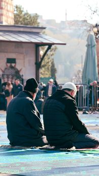 Two men seated outdoors in prayer at sunrise, cityscape background.