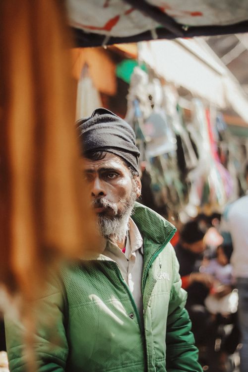 Free A man in a green jacket stands in a lively outdoor market with blurred shoppers. Stock Photo