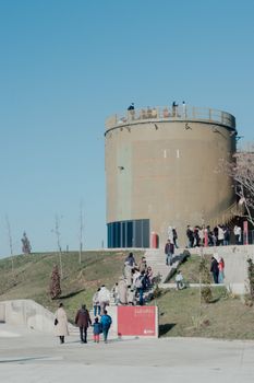 People gathering at the outdoor cultural site in İstanbul, featuring a cylindrical structure and clear blue sky.