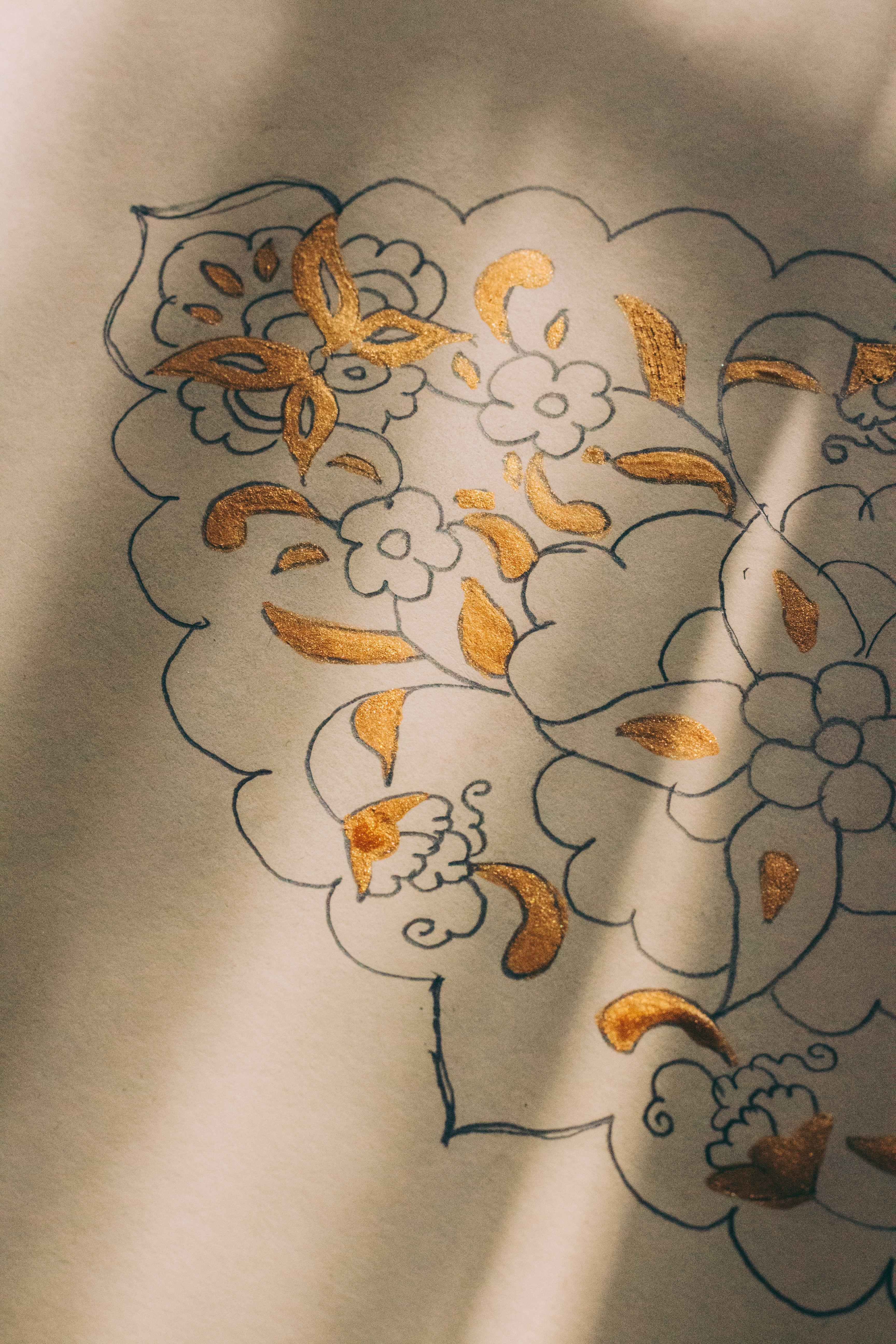 Detailed floral artwork with gold accents on paper, softly lit.