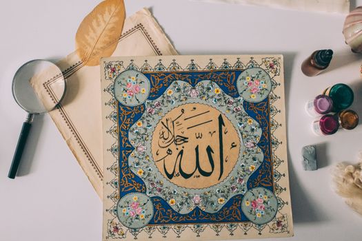Beautiful Islamic calligraphy artwork surrounded by creative tools on a flat lay setting.