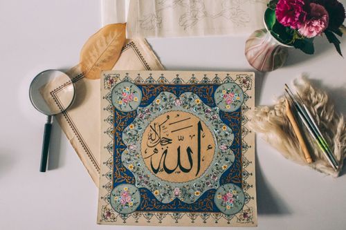 Free Intricate Islamic calligraphy surrounded by art tools and flowers on a table. Stock Photo