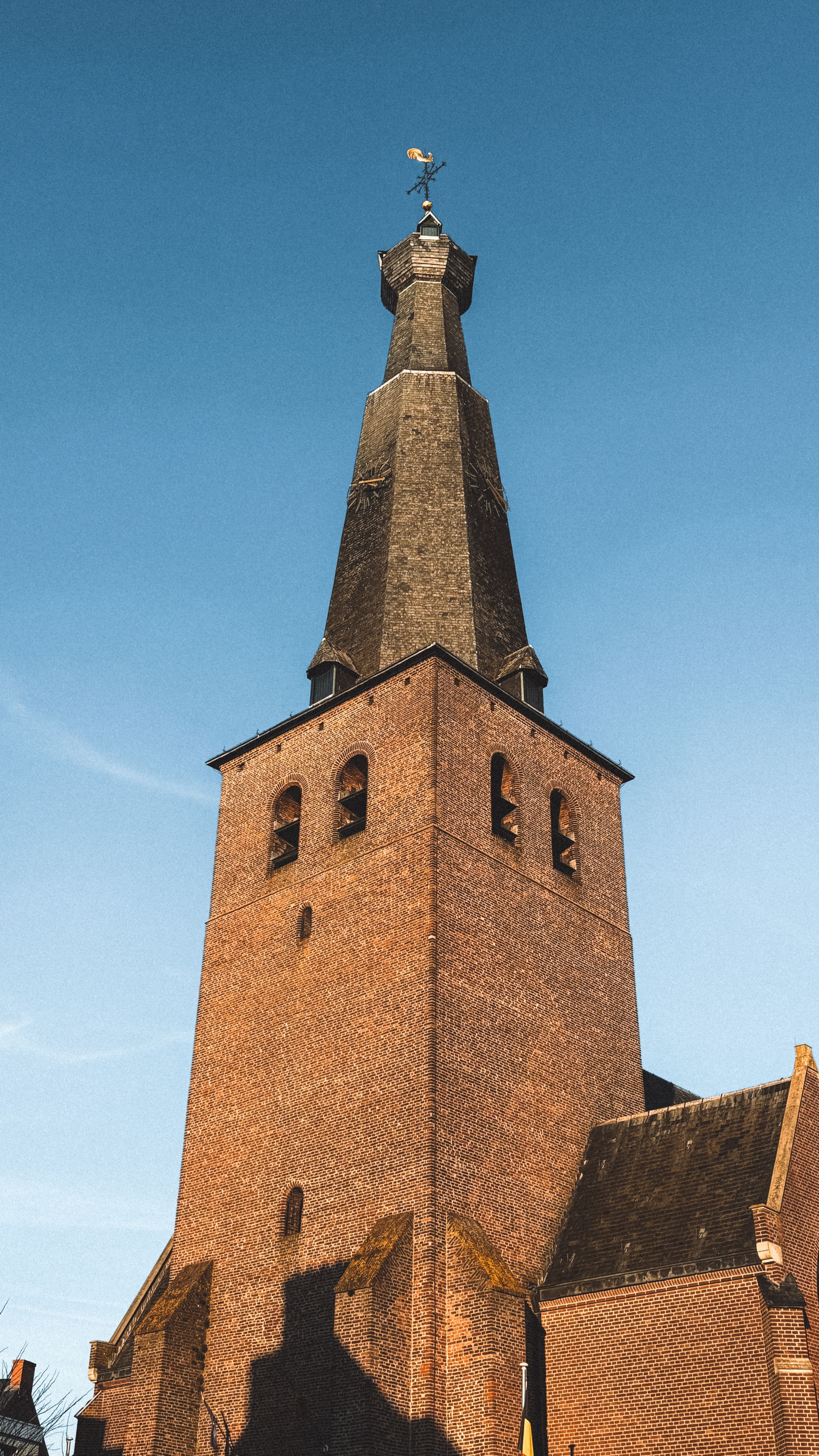 Brick church tower and spire photographed from below against a clear blue sky.