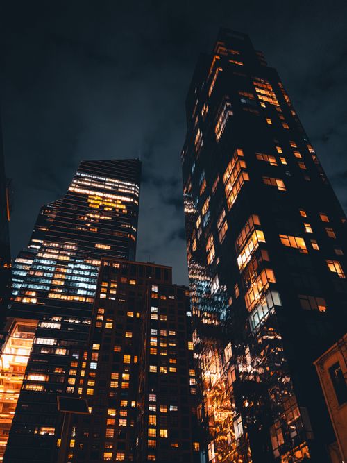 Free Dramatic view of urban skyscrapers lit up at night, with warm light reflecting off tall buildings. Stock Photo