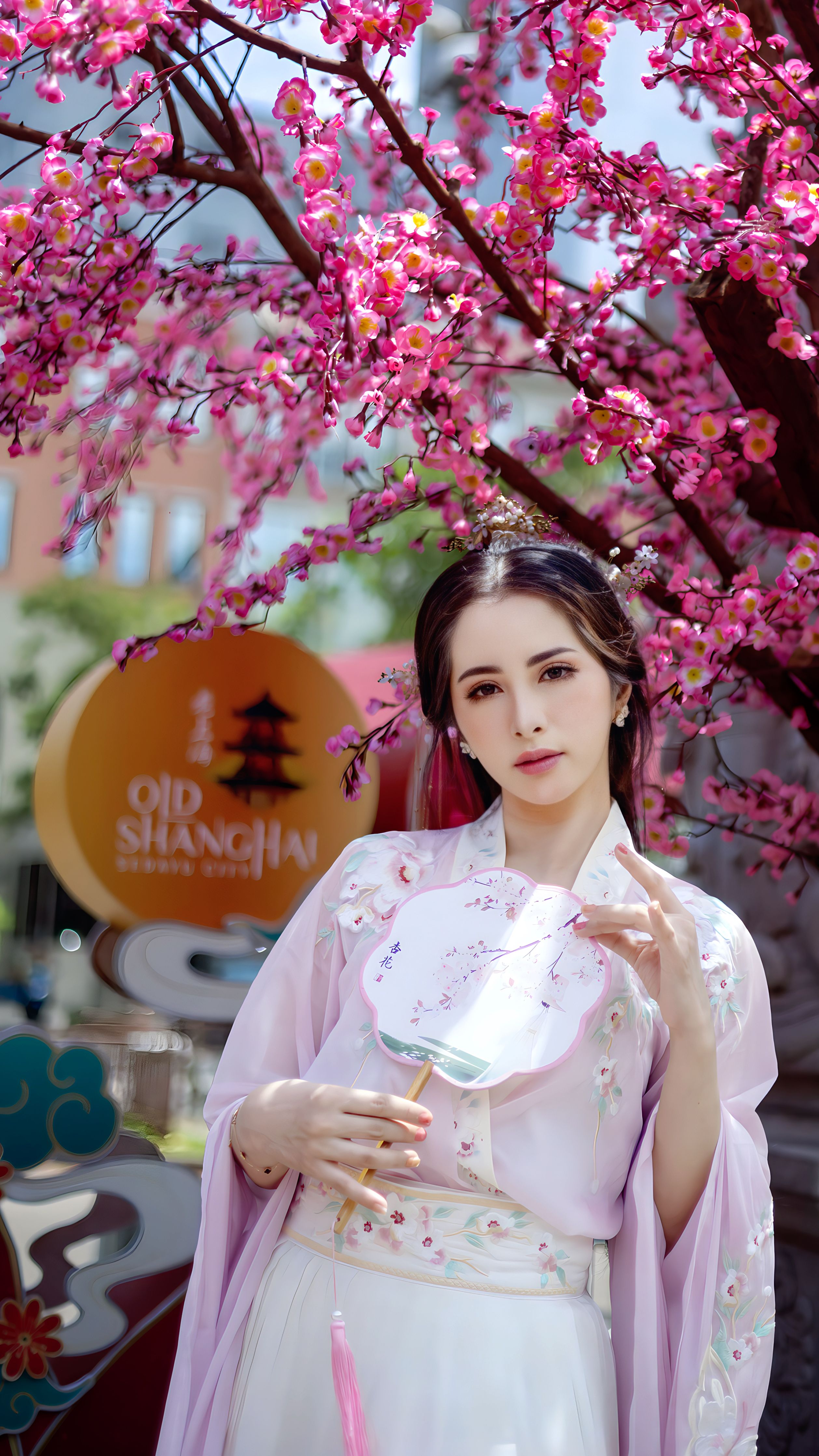 Woman in traditional attire under pink blossoms in Jakarta.