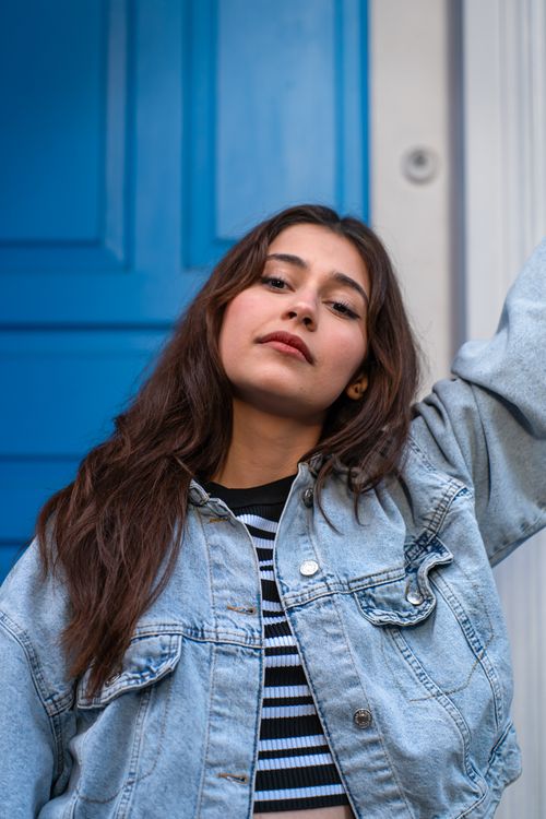 Free Casual portrait of a young woman posing confidently with a blue door backdrop. Stock Photo