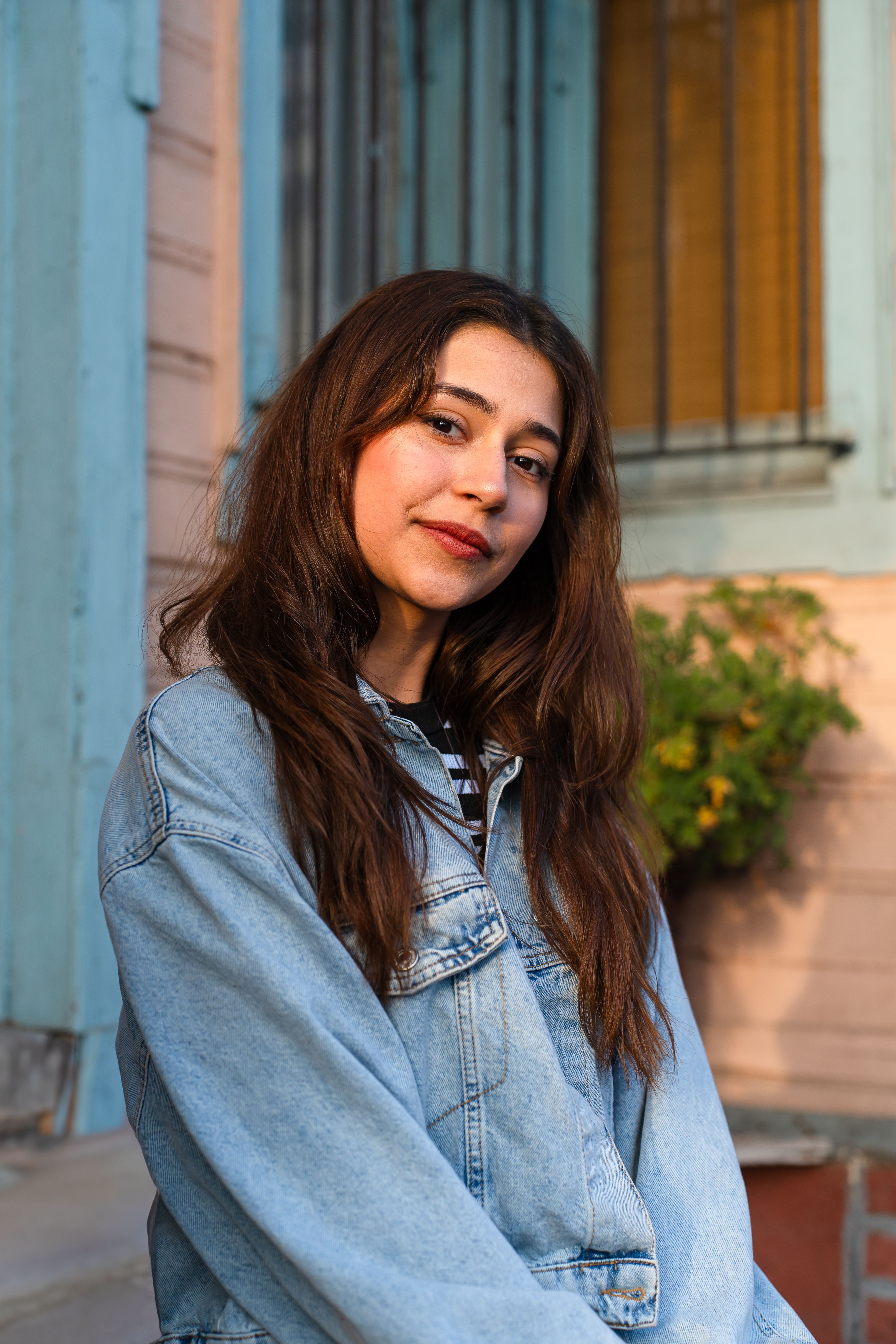 Portrait of a young woman in a denim jacket smiling outdoors.