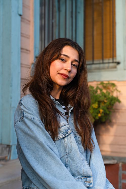 Free Portrait of a young woman in a denim jacket smiling outdoors. Stock Photo