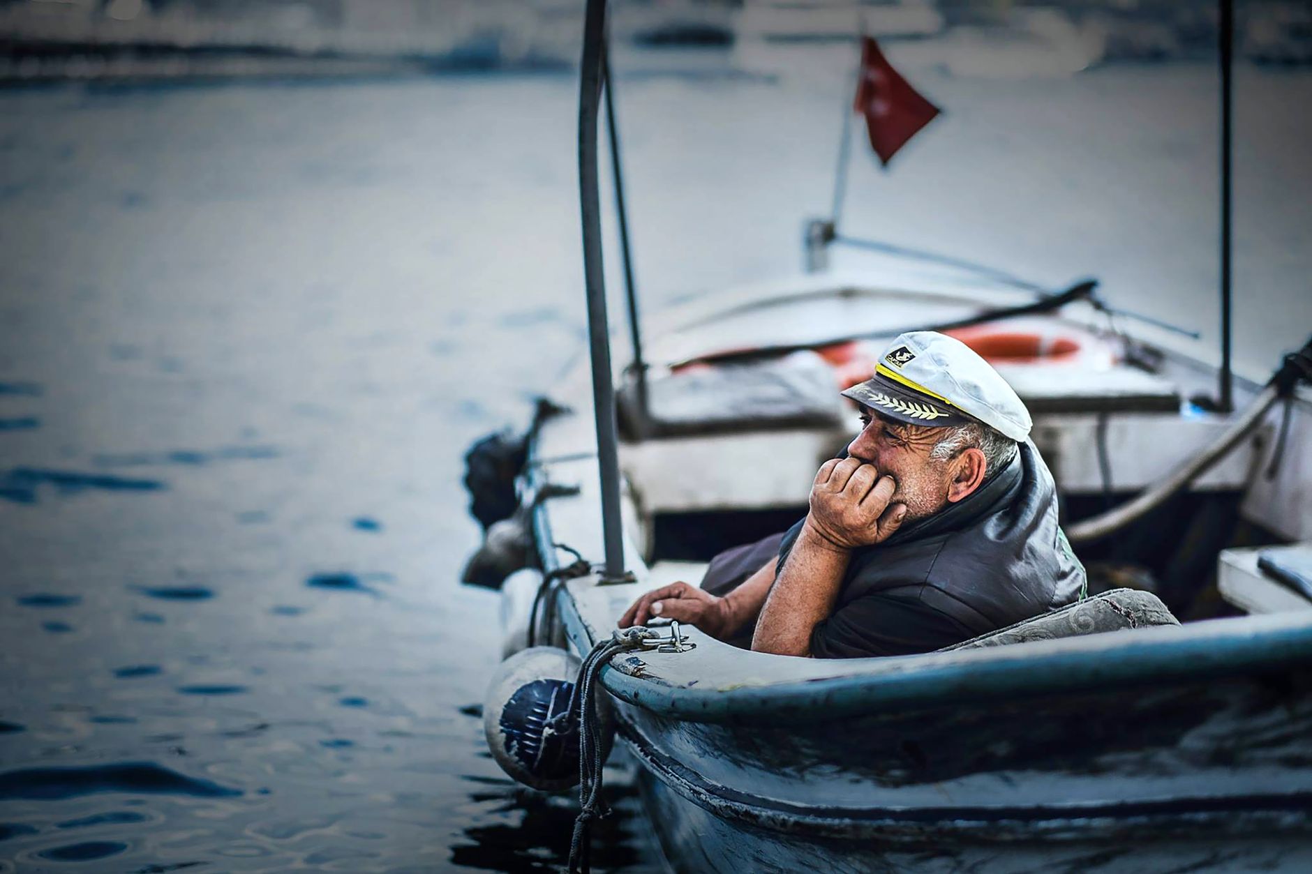 Elderly sailor in a boat gazing thoughtfully at the sea with a distant horizon background.