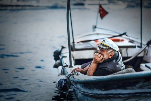 Elderly sailor in a boat gazing thoughtfully at the sea with a distant horizon background.