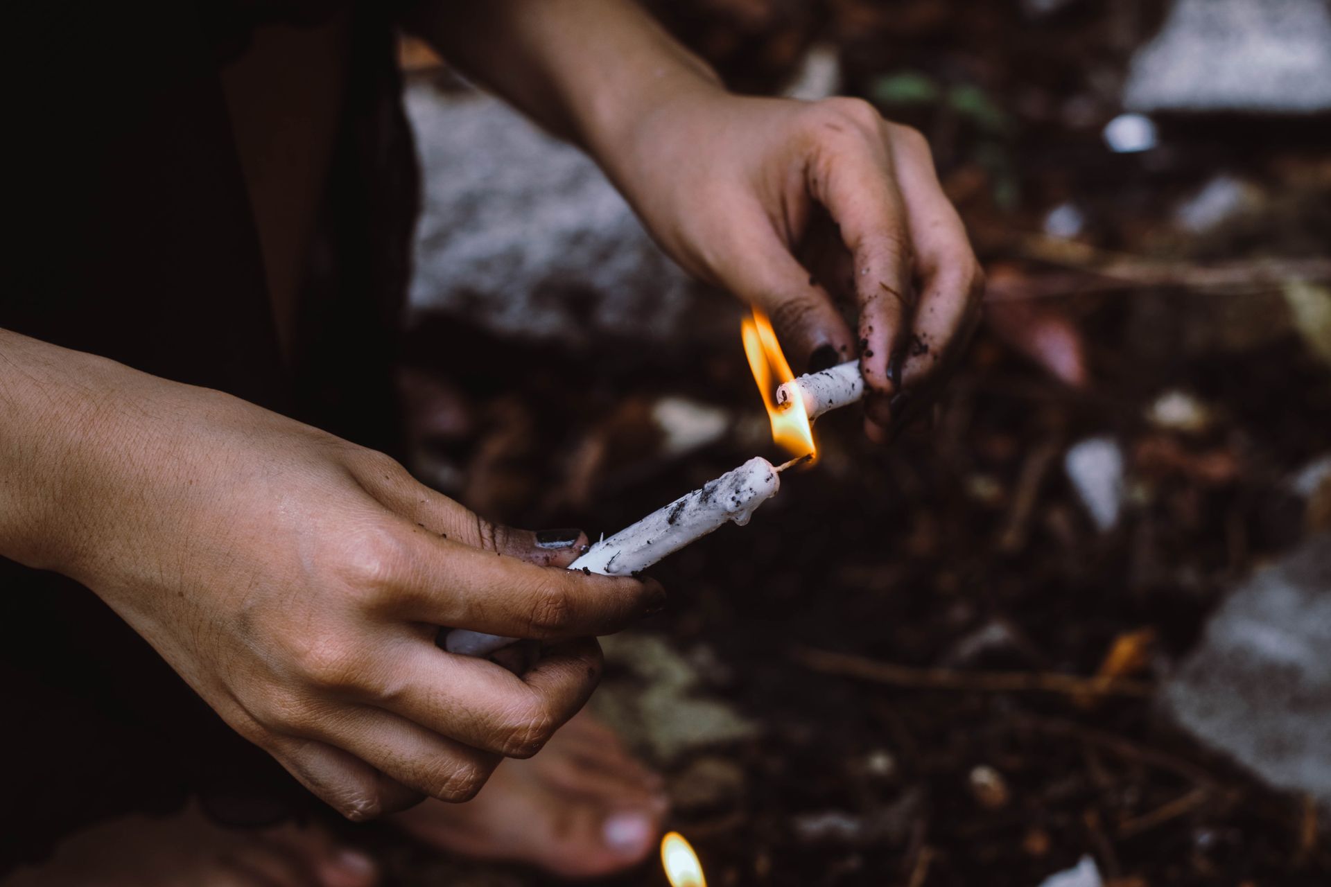 A person lighting white candles outdoors, focusing on hands and flame against a natural background.