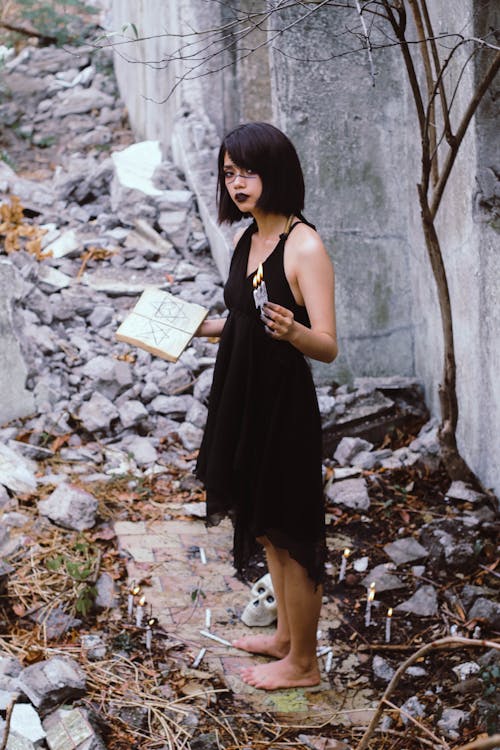 Woman in Black Sleeveless Dress Holding White Book Standing Outdoors