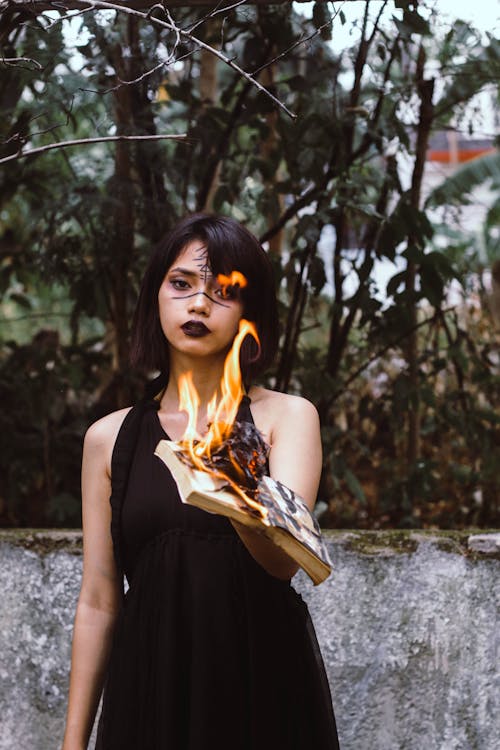 Free Woman Wearing Black Sleeveless Dress While Holding Burned Book Stock Photo