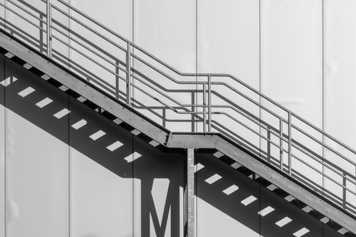 Free A striking black and white photo of an outdoor metal staircase casting geometric shadows on a wall. Stock Photo