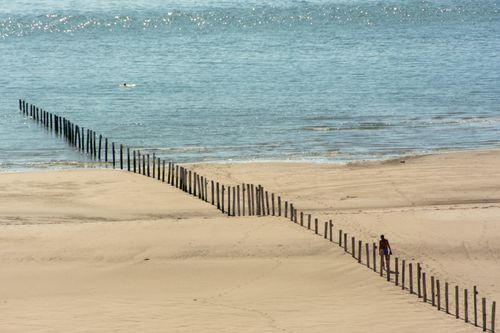 Free A lone person walks along wooden pilings on a wide sandy beach stretching into the ocean. Stock Photo