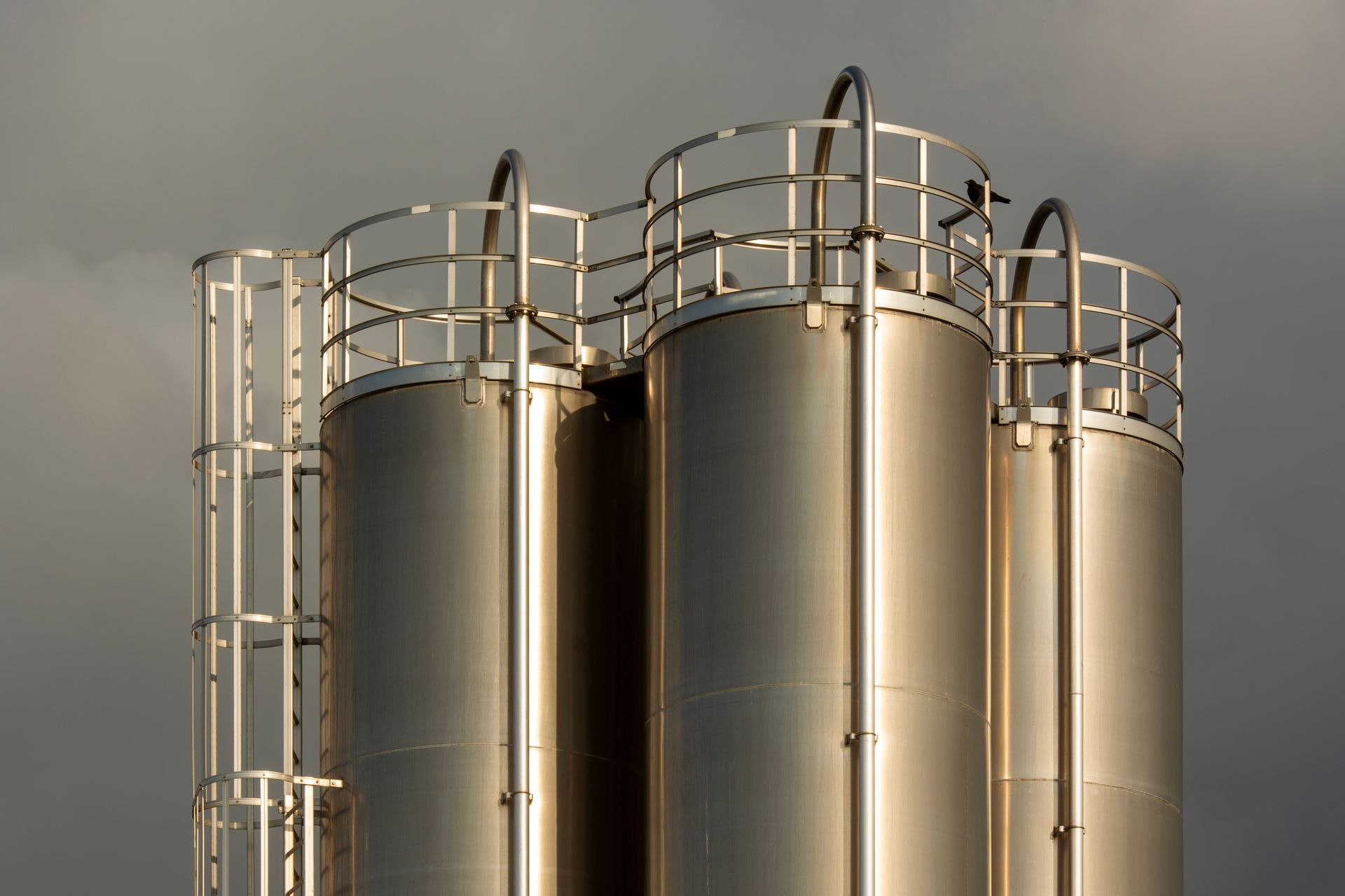 Close-up of industrial metal storage tanks against a backdrop of dark clouds, creating a dramatic industrial scene.